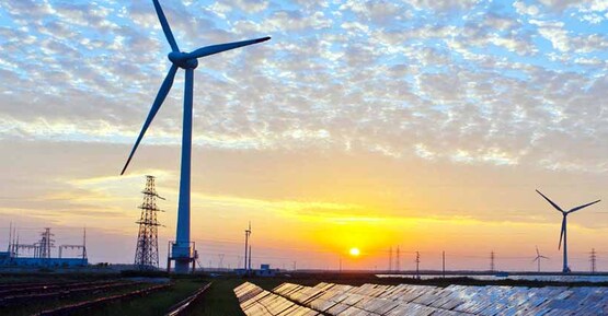 solar panels in foreground, wind turbines in middle ground, and the electric grid in the background