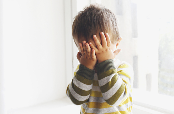Upset child covering his face at home. 
