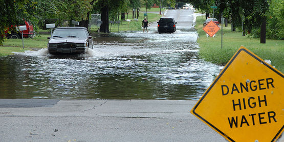 Oklahoma, Okla., August 19, 2007 -- Cars drive though a flooded street carefully after heading the High Water Danger Signs. FEMA has a preparedness program to make people aware of the dangers of driving though flooded roads. 