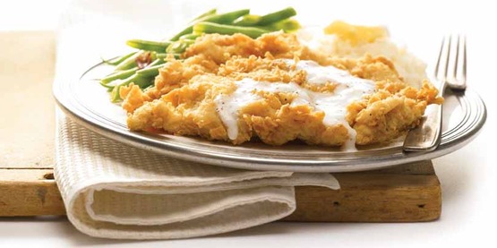 a plate with fried chicken, gravy, biscuit, green beans