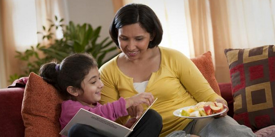 A woman and her daughter read and share a snack together.