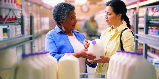 Two women at a supermarket discuss a milk label