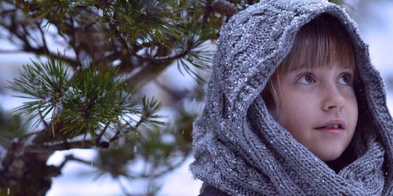 child in knit hood outdoors in the winter before an evergreen
