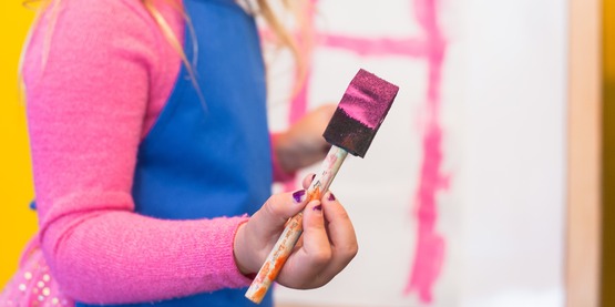 A child holding a sponge brush with pink paint on it. 