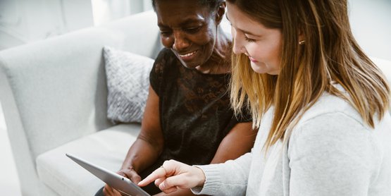Younger woman helping senior on tablet. 