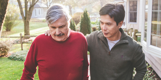 Two men walking. The younger man's arm is around the older man's shoulder. 