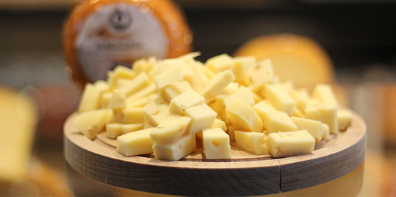 cubes of cheese on a cheese board, blurry round of cheese in background