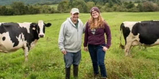 Two people standing in field with two cows.