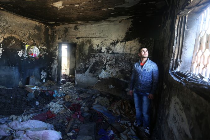 A relative stands in the burnt-out shell of West Bank home where a Palestinian family was killed in a firebomb attack by suspected Jewish extremists.
