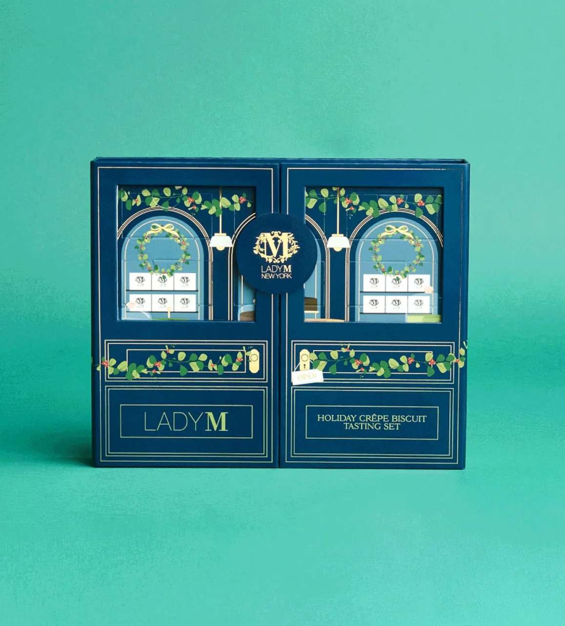 Navy blue Lady M Holiday Crêpe Biscuit Tasting Set gift box designed to resemble a boutique storefront with decorative windows and greenery