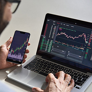 Image of a man using phone and laptop to track stocks
