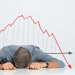 Image of a frustrated investor laying his head on his desk in front of a falling stock chart