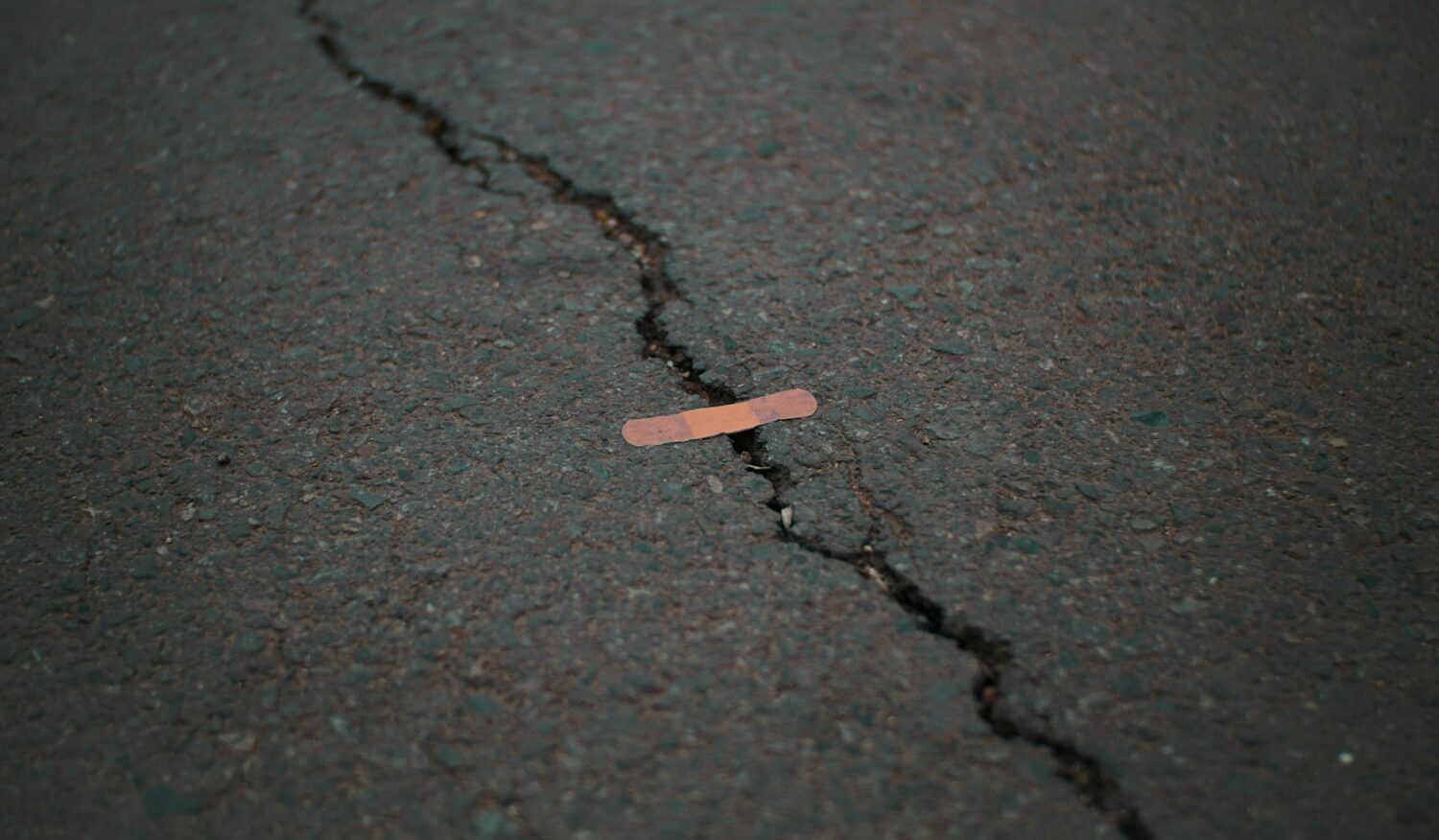 Small pink band-aid across large crack in road.