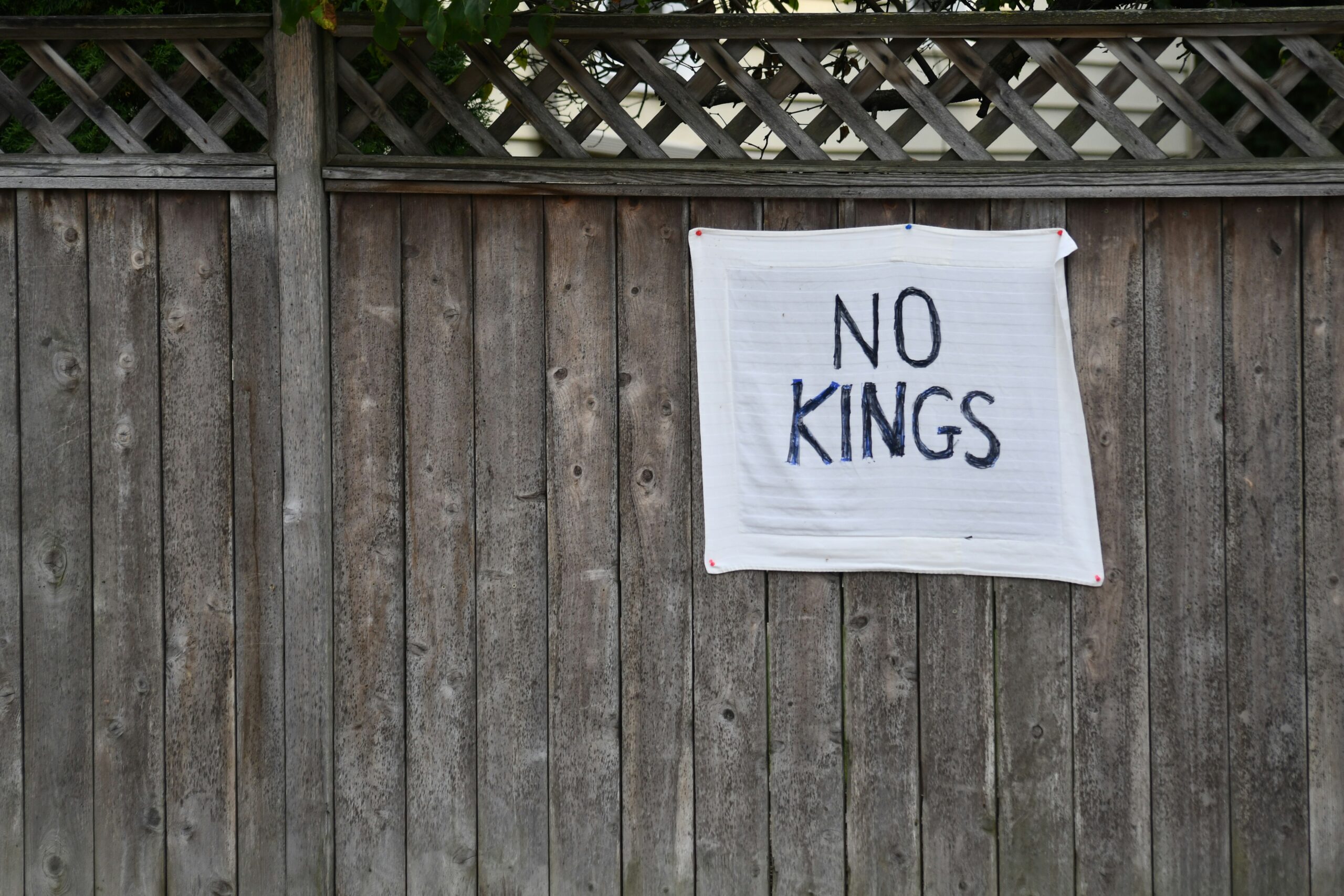 A handwritten "no kings" sign attached to a weathered wooden fence