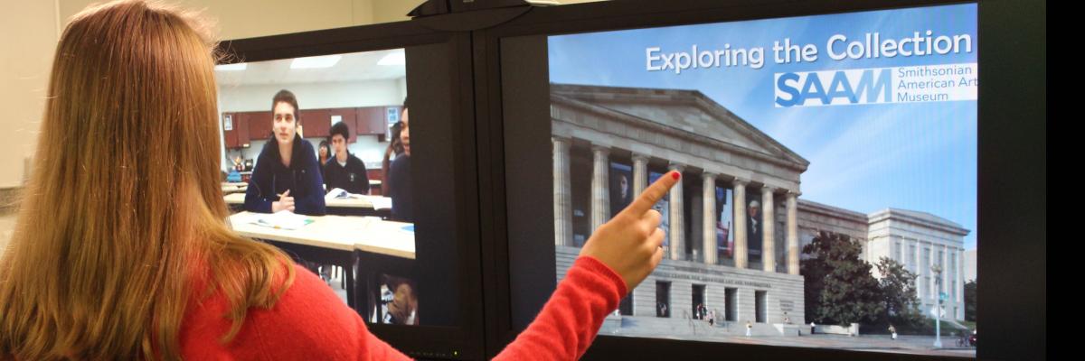 A photograph of a woman talking to a classroom remotely while also showing them a powerpoint on a split screen.
