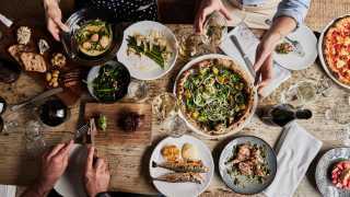 This is a photo of people enjoying a food spread of pizza, asparagus, fish, bread, olives and wine at the Wilding restaurant in Oxford.