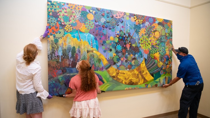 Several students carefully hanging a large painting in an exhibit
