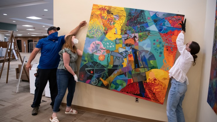 Several students carefully hanging a large painting in an exhibit