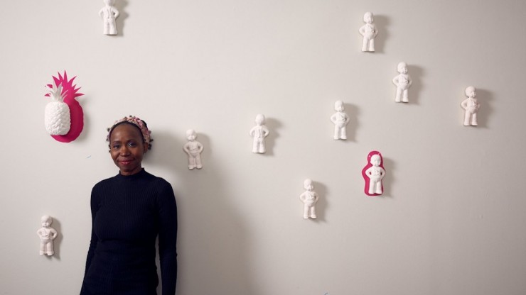 Artist, Sharon Norwood, stands in front of her exhibit, statues of babies on a wall