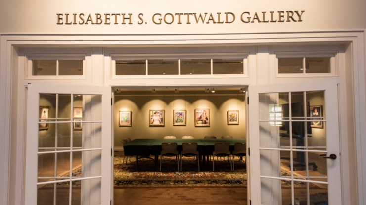 The entrance to a gallery with white doors, paintings can be seen inside of it