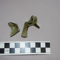 This green 18th century pharmaceutical glass is smooth to the touch and has two separate pieces--one being a part of the short neck and the other making up the body of the  bottle.