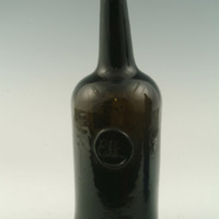 An example of an fully in-tact early 19th century wine bottle with a long neck and body, made of dark green glass. Students of the time would have stored their wine in these bottles.