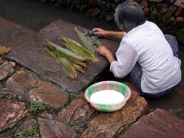 A villager washing bamboo leaves and rice at the ditch flowing through the village