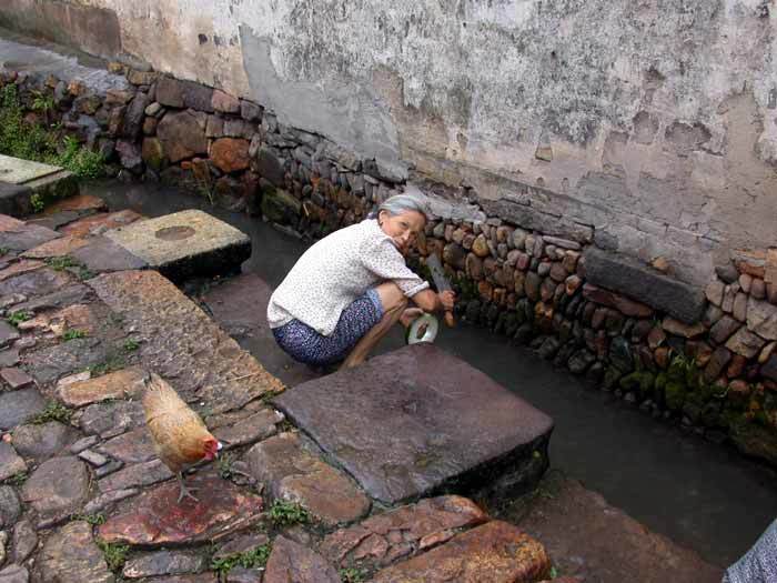 A villager washing a slice of winter melon at the ditch flowing through the village