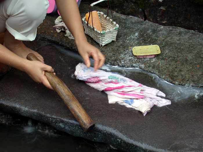 A villager using a pestle to wash clothes at the ditch flowing through the village-1