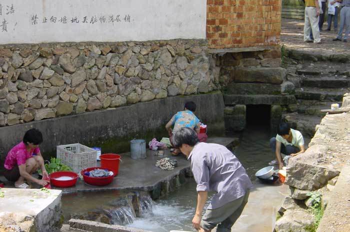 Villagers washing clothes, vegetables in the ditch flowing through the village