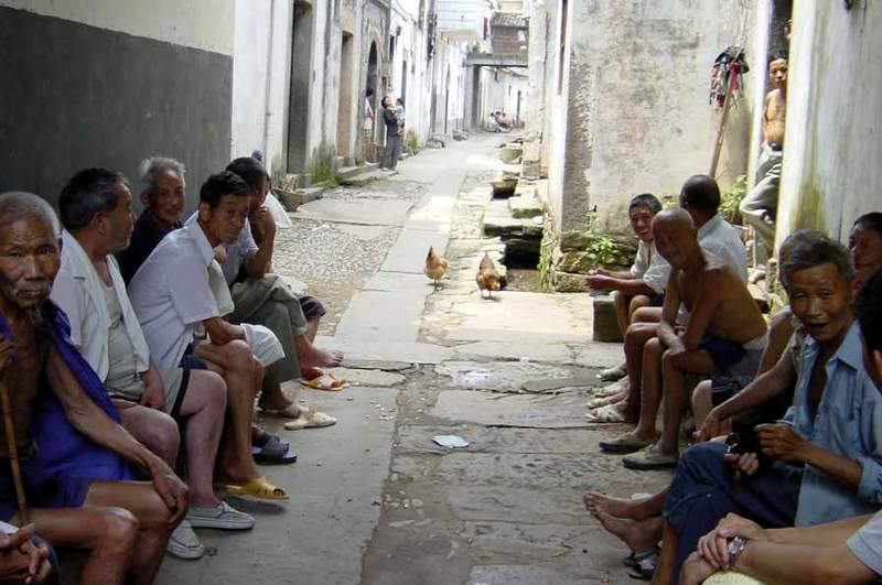 Street scene-villagers sitting and chatting on the sides of street Street scene-villagers sitting and chatting on the sides of street