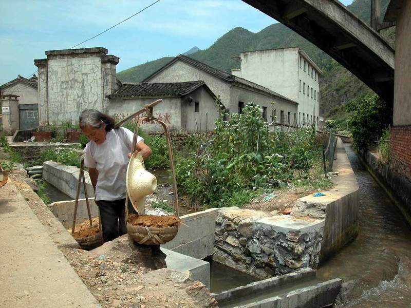 A woman working, carrying a pole with two baskets A woman working, carrying a pole with two baskets