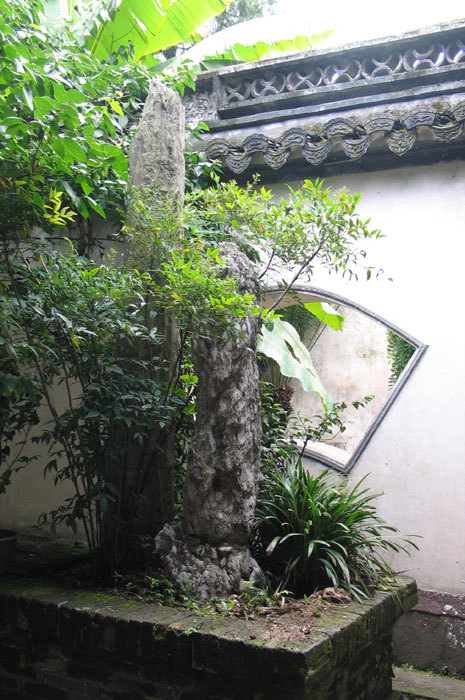 view of fan-shaped window with miniature landscape -- tai hu rock, nandina, and reedy grass