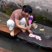A villager using a pestle to wash clothes at the ditch flowing through the villag