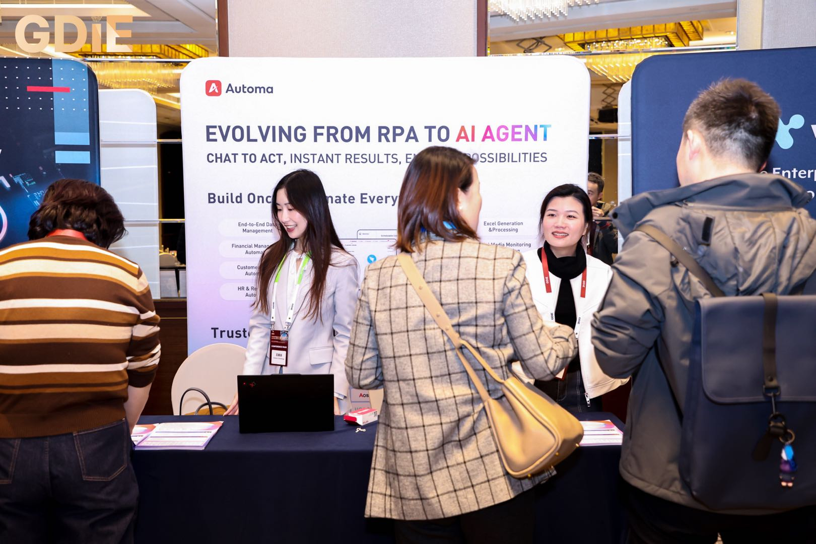 Professional attendees interacting with staff at the Automa booth during GDIE 2026, focusing on the "Chat to Act" agentic automation display.