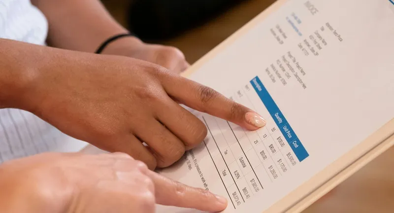 Two hands pointing at an invoice showing quantity price and total cost calculation