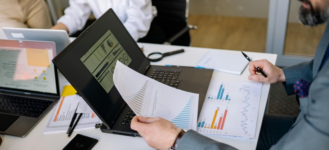 A businessman analyzing automated data reports on a laptop and paper, showcasing data extraction automation workflow.
