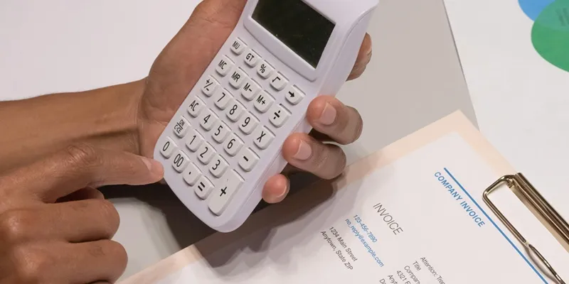 Hand using a white calculator on an invoice and financial documents for budgeting