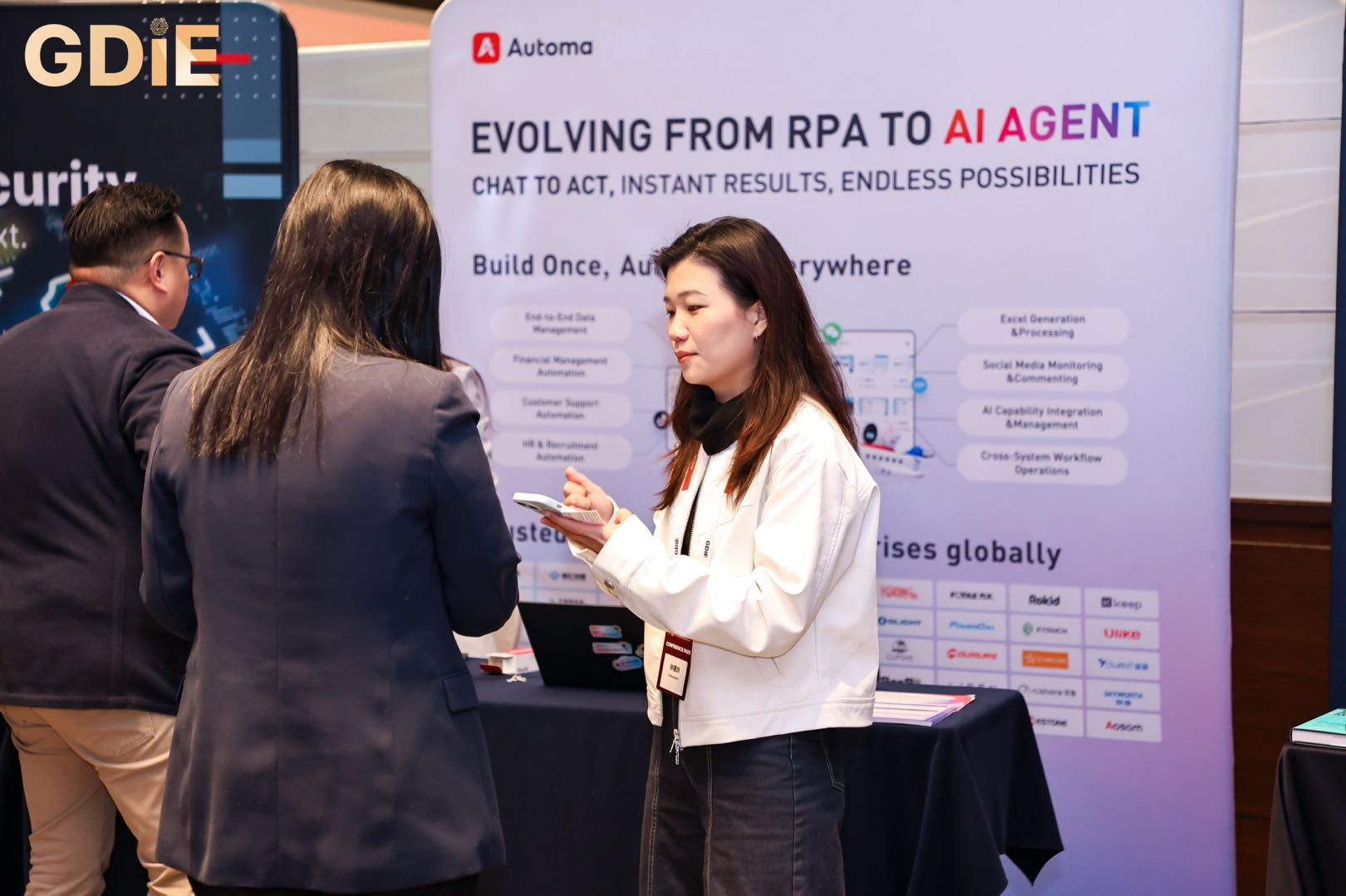 An Automa staff member providing a live mobile demonstration of agentic automation technology to a visitor at the GDIE 2026 exhibition booth.