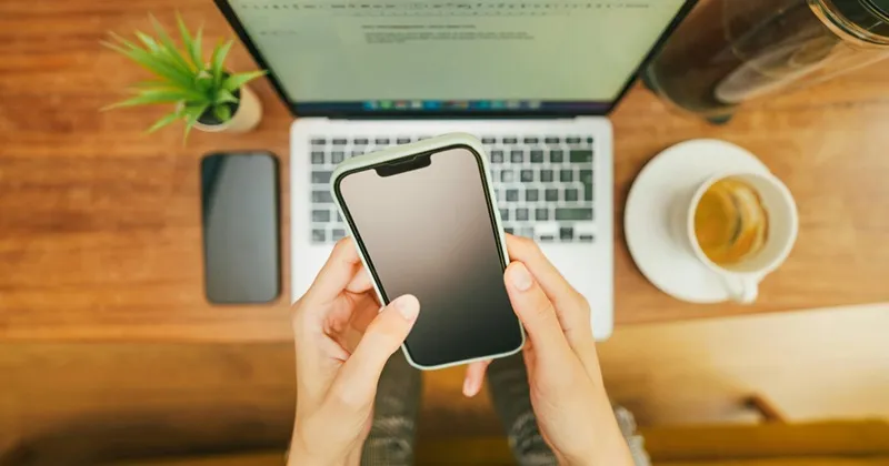 Hands checking a smartphone and laptop for email automation performance reports