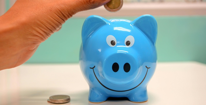 Hand depositing a coin into a piggy bank