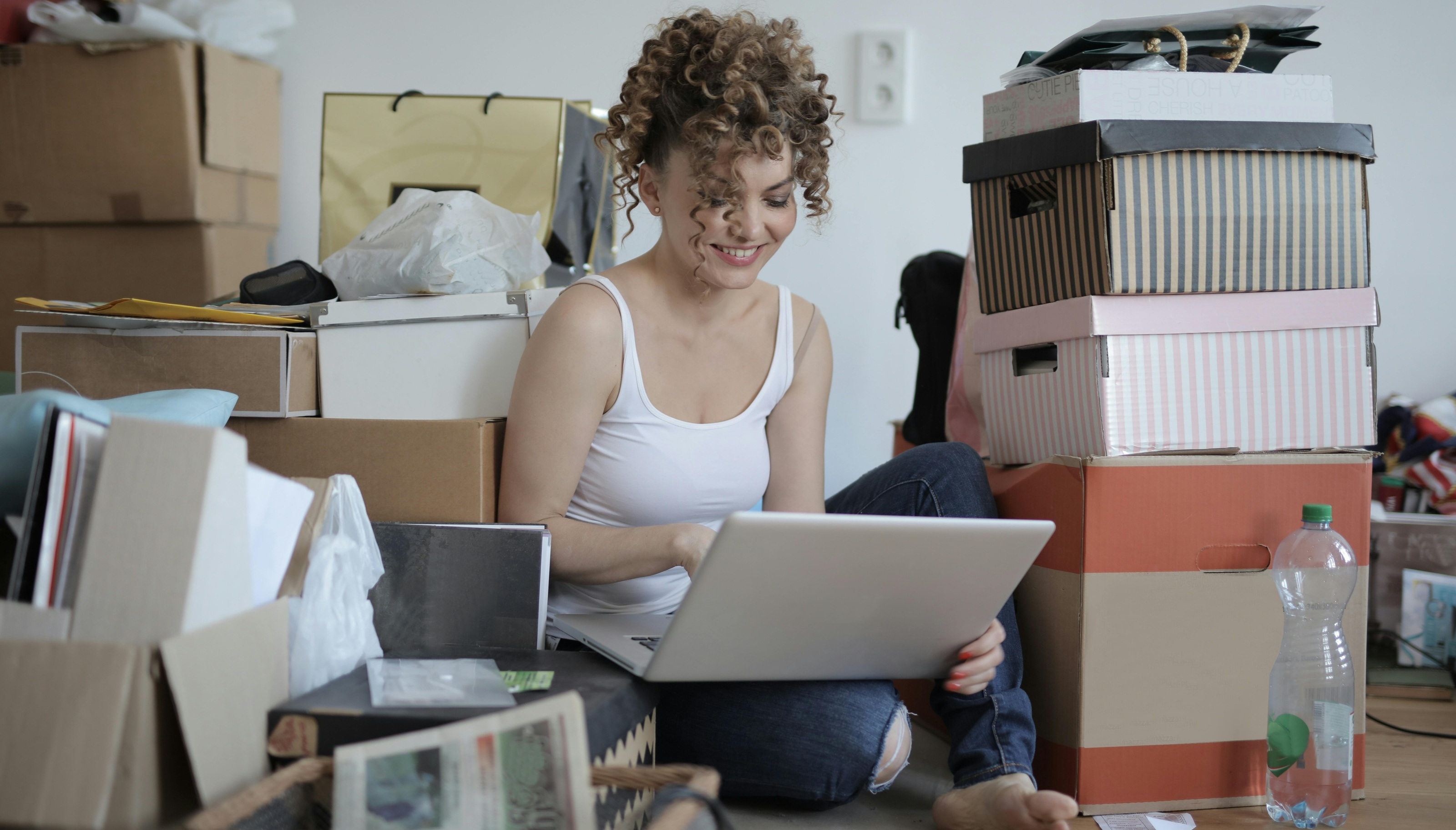 A smiling entrepreneur using a laptop surrounded by packages, showcasing the efficiency of eBay automation for order fulfillment.