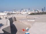 Smurf walking in Bahrain fort with Manama skyline behind