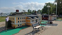 De minigolfbaan op de camping met gebouwen in het klein van de stad