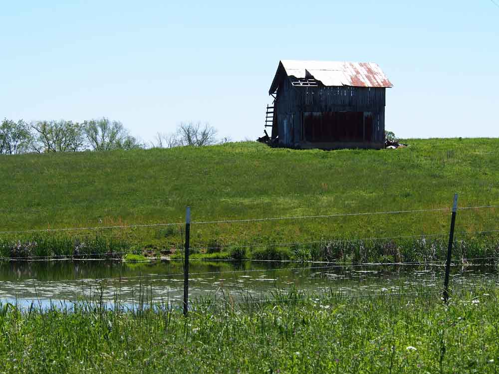 Original image of black barn with white metal roof on top of hill