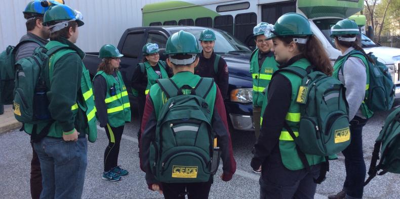Group of people standing in a circle in green neon vests and hard hats