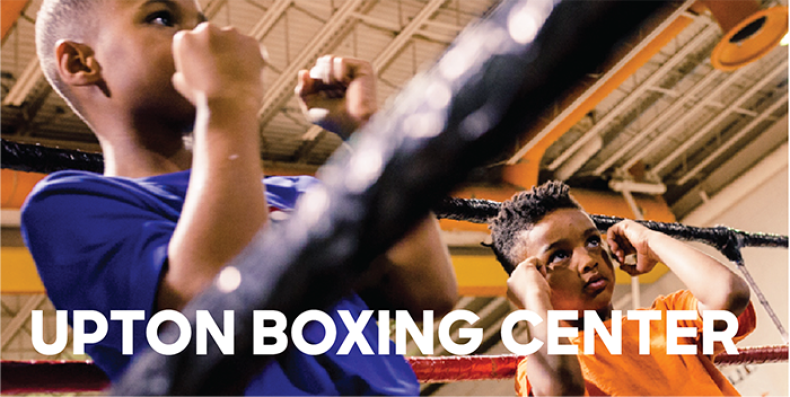 Two young boys hold up fists in a boxing ring.