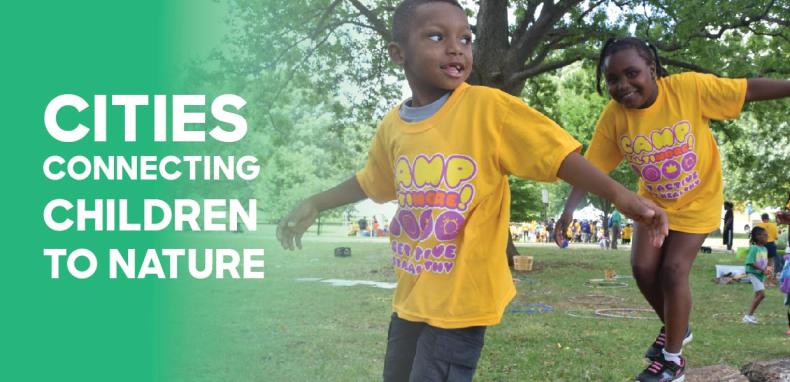 Two children in bright yellow T-shirts Play "airplane." Next to them are the words, "cities connecting children to nature."