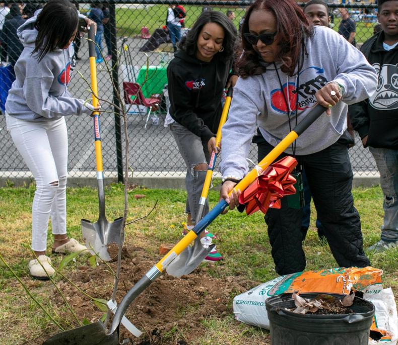 Three women outdoors using shovels to dig in the earth.