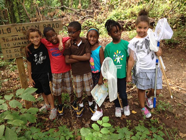 Six children stand in a garden area, posing for a photograph.